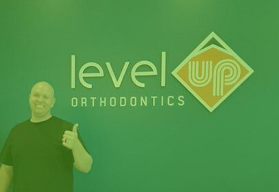 A man standing beside the level orthodontics signage is making a thumbs-up gesture.